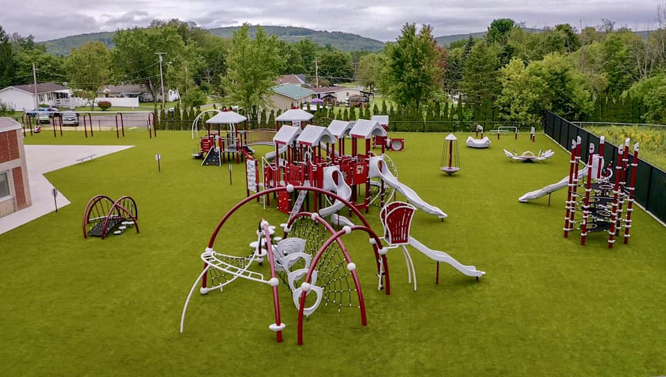 Overview of red and white playground equipment in large grassy area