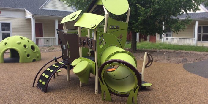 Photo of a play structure with climbers, a slide, and play panels, and a textured play dome for climbing or hiding in the background
