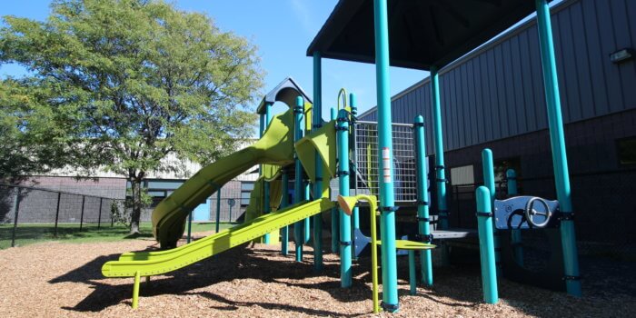 Photo of a multi-level play structure with multiple slides and climbers, and shaded by a large roof overhead