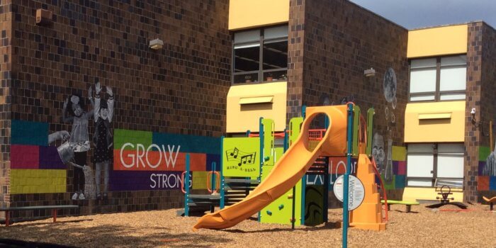 Photo of a colorful playground with a main structure and some independent components, installed next to murals on the school building