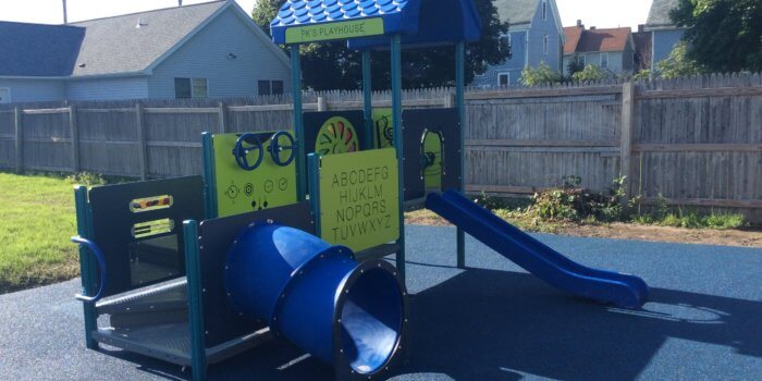 Photo of a small play structure with decks, a slide, and a tunnel on unitary surfacing