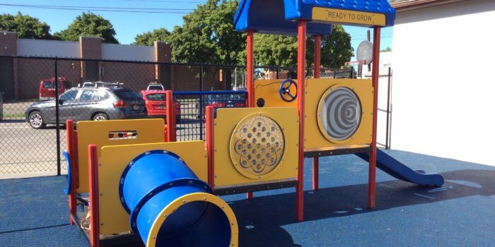 Photo of a small play structure in primary colors with decks, a slide, and a tunnel