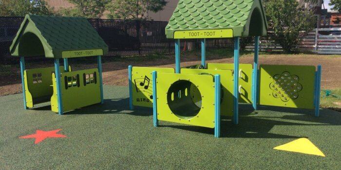 Photo of play structures with play panels, roofs, and a play table on unitary surfacing