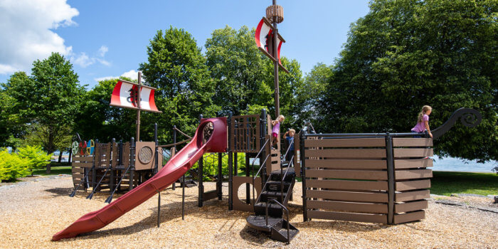 Photo of a ship inspired play structure with numerous climbers, sails, and a slide