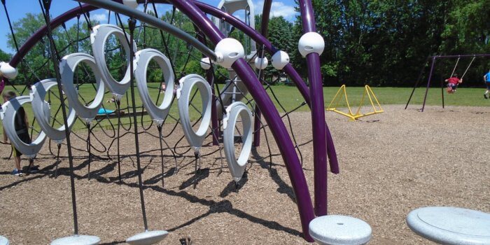 Photo of playground with swings and large climbing structure with multiple components.