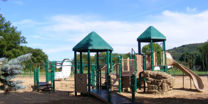 Photo of playground with climbers, slides, decks, and curved climbing wall.