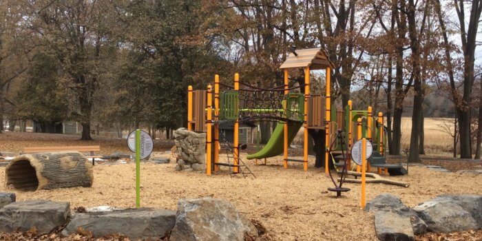 Photo of a play structure withs several decks and climbers and a log tunnel.