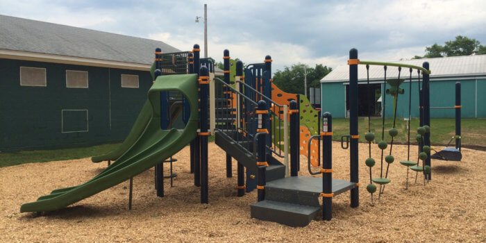 Photo of playground with slides, climbers, and rope step bridge.