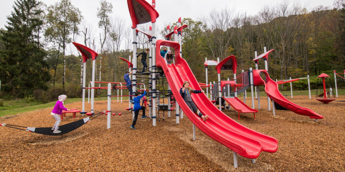Photo of children playing on a tall slide structure, with other playground components visible