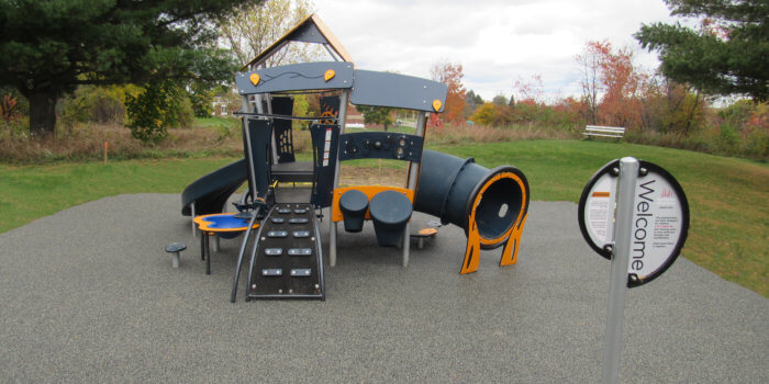 Photo of a small play structure for 2-5 year olds, featuring a bongo panel, a play table, a slide, and climbers