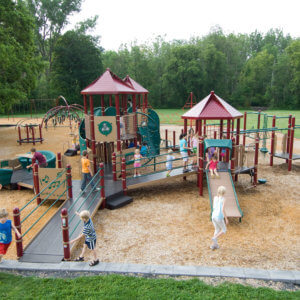 Photo of children playing on a large play structure with several ramps, decks, and roofs, and many climbers and slides