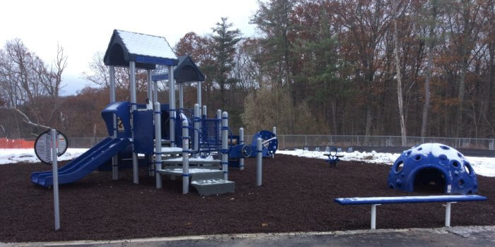 Photo of snow covered playground structure with independent components, including a sensory dome, planet shaped climber, and spring rider.