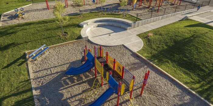 Photo of a large play area with two separate playground structures, several independent play components, and bench seating built into the topography