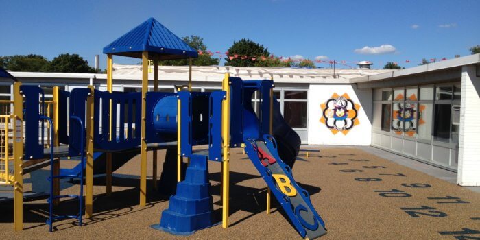 Photo of a playground in a schoolyard with slides, tunnels, and climbers.