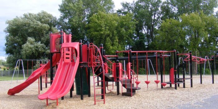 Photo of red and black playground with multiple levels of decks, slides, and climbers