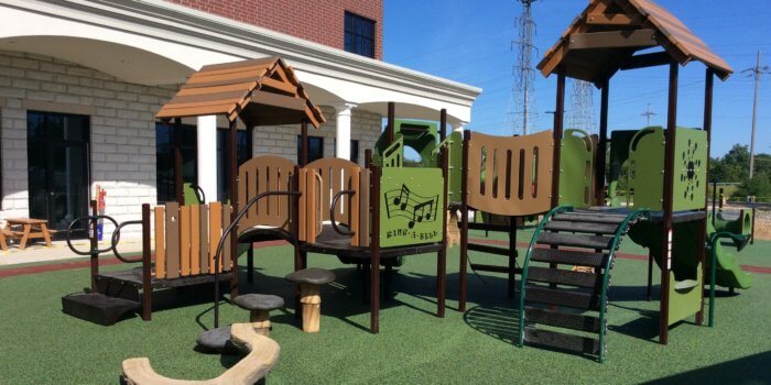 Photo of nature inspired playground, with log balance beam, play panels, and faux wood roofs.