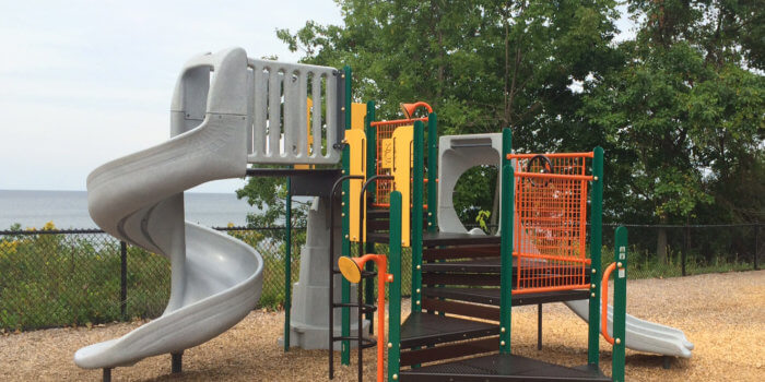 Photo of play structure with multiple decks, slides, and climbers overlooking the water