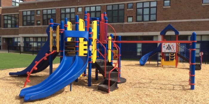 Photo of play structure with slides and climbers in front of a school building.