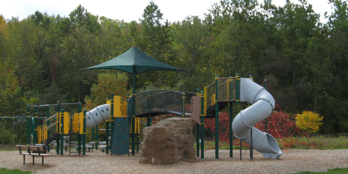 Photo of play structure with slides, rock climbers, bridges, and a shade covering