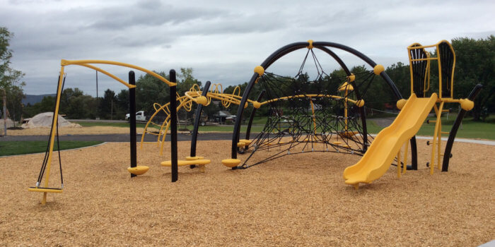 Photo of playground with curved climbing structure, slide, and spinner.