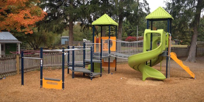 Photo of a play structure with slides, climbers, a bridge, and overhead play components.