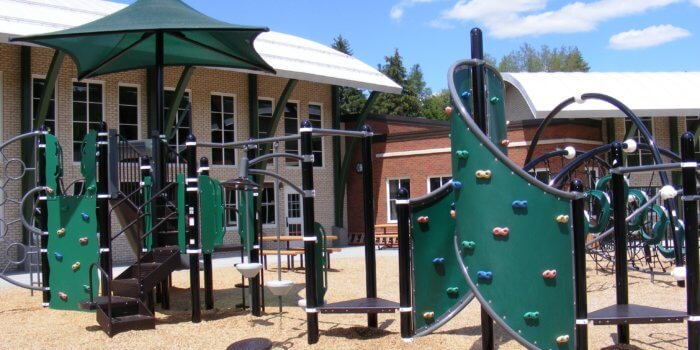 Photo of playground with curved climbing walls, shade structure, slides, and climbers.